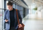 Man on smart phone - young business man in airport. Casual urban professional businessman using smartphone smiling happy inside office building or airport. Handsome man wearing suit jacket indoors.